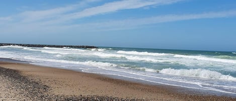 A beach with waves, pebbles, and a clear sky.