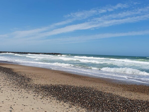 A beach with waves, pebbles, and a clear sky.