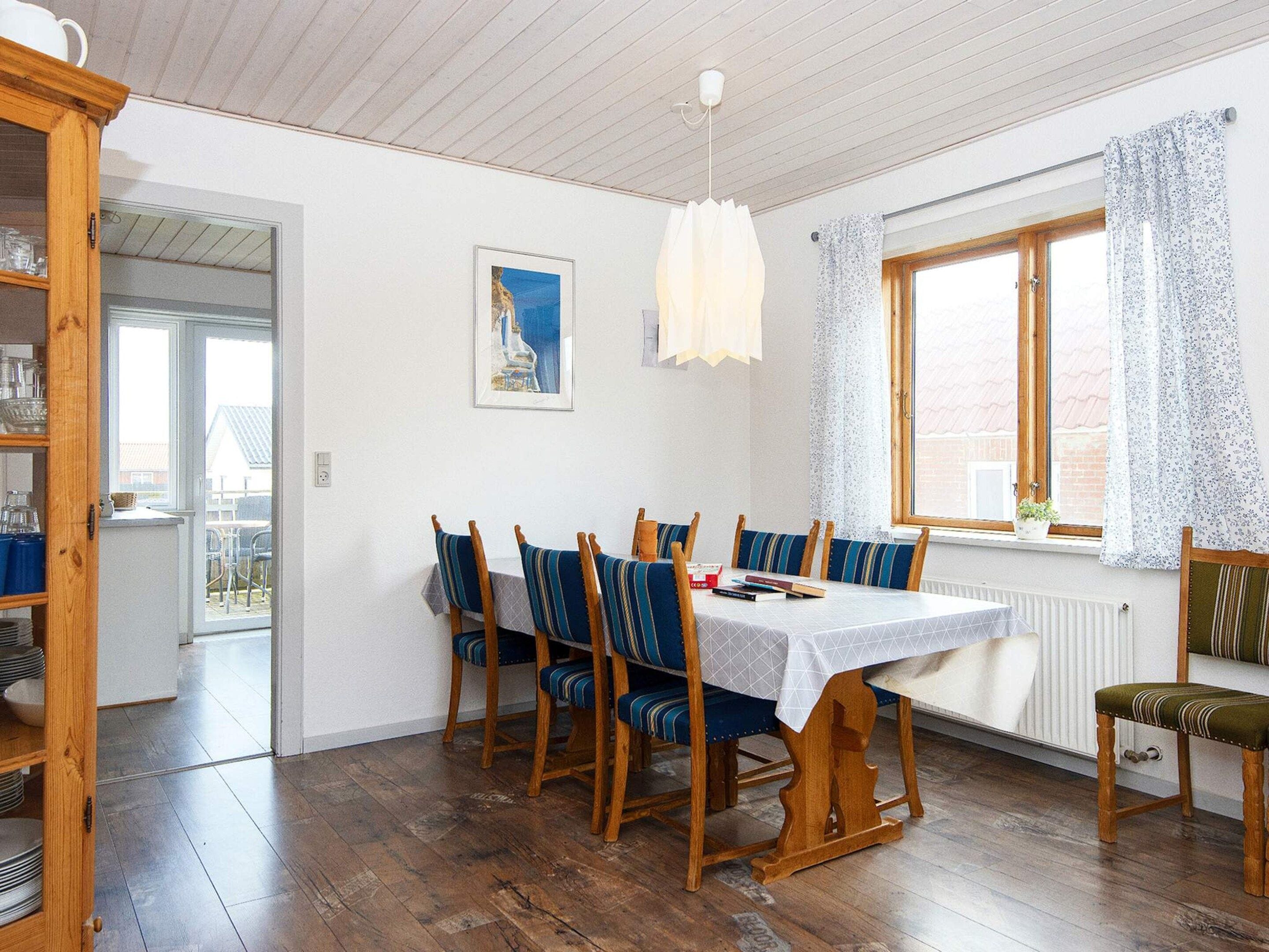 A dining area with a wooden table and chairs, a window with curtains, and a view of the outside.