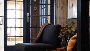 Una stanza con una poltrona dai toni scuri, un tavolino con un vaso di fiori e una porta in legno con vetrate.