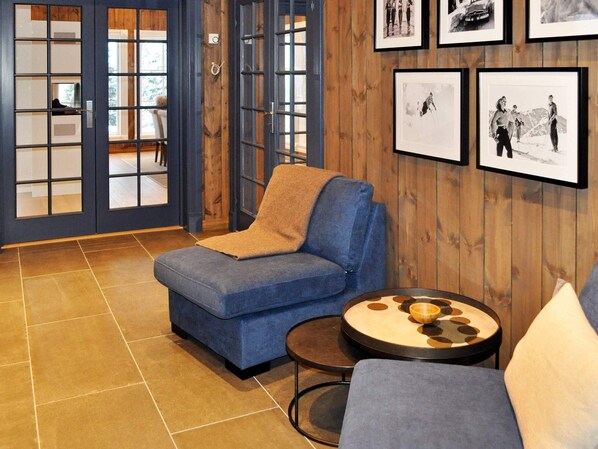 A room with a blue armchair, a round table with a bowl, and a wooden wall with framed pictures. - Holiday Home in FÃ¥vang (Ringebu)