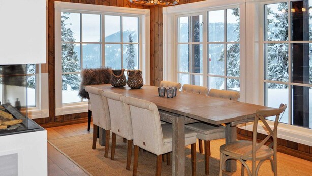 Una sala da pranzo con pannelli in legno, un tavolo grande e sedie, ampie finestre con vista innevata e un lampadario.