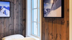 Una camera da letto con pareti in legno, un letto con biancheria bianca e due quadri incorniciati raffiguranti paesaggi montani innevati.