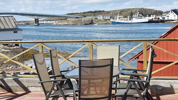 A deck with outdoor seating overlooking a body of water, a bridge, and a coastal town.