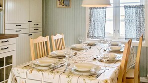 A dining table set for six with floral tablecloths, wooden chairs, and a window with patterned curtains.