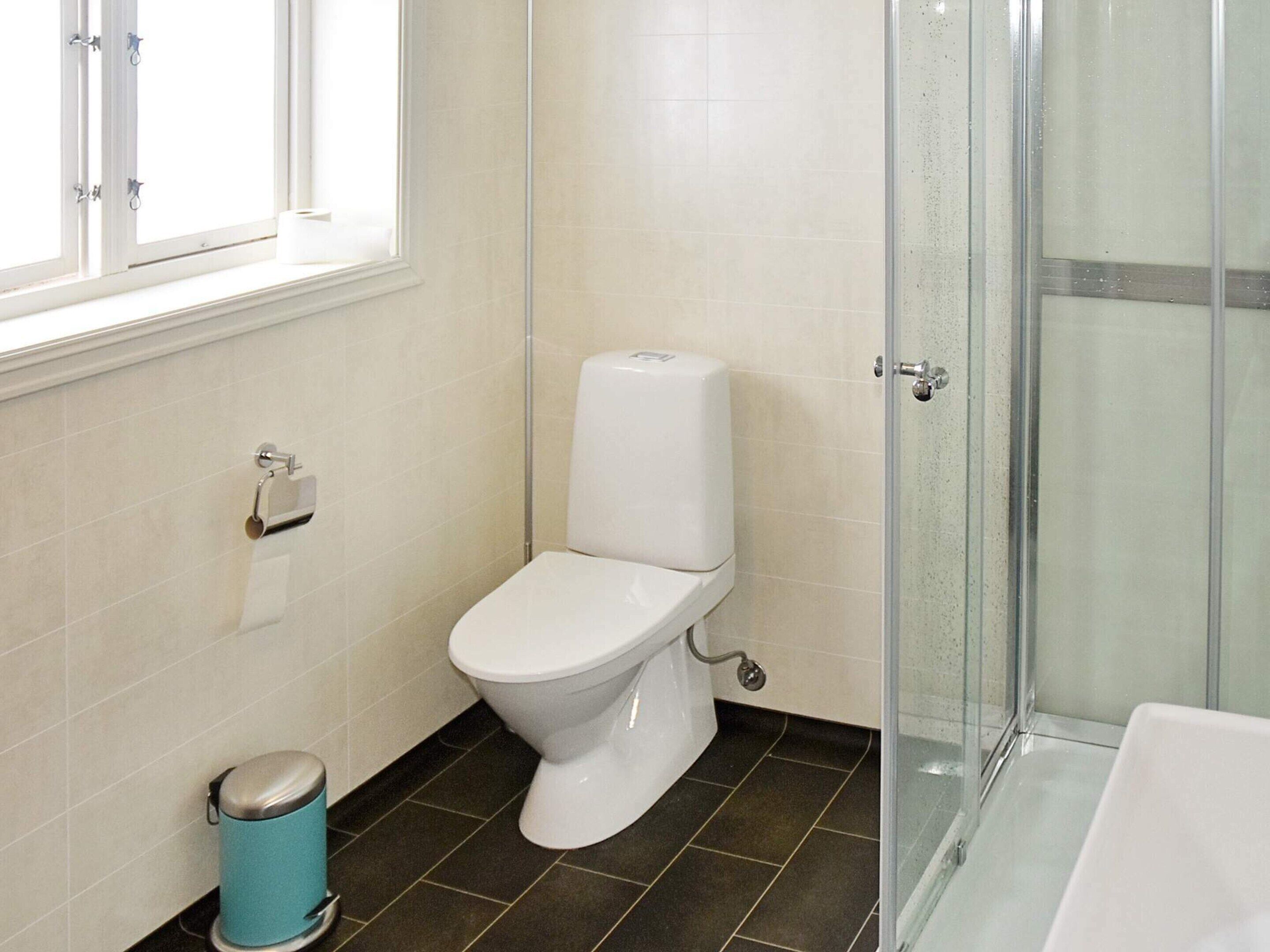 Een badkamer met een toilet, een prullenbak en een douchecabine met glazen wanden.
