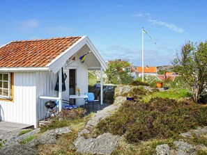 A white building with a red-tiled roof, a small porch with a table and chairs, and a flagpole in the background. - 2 Person Holiday Home in Gullholmen (Gullholmen)