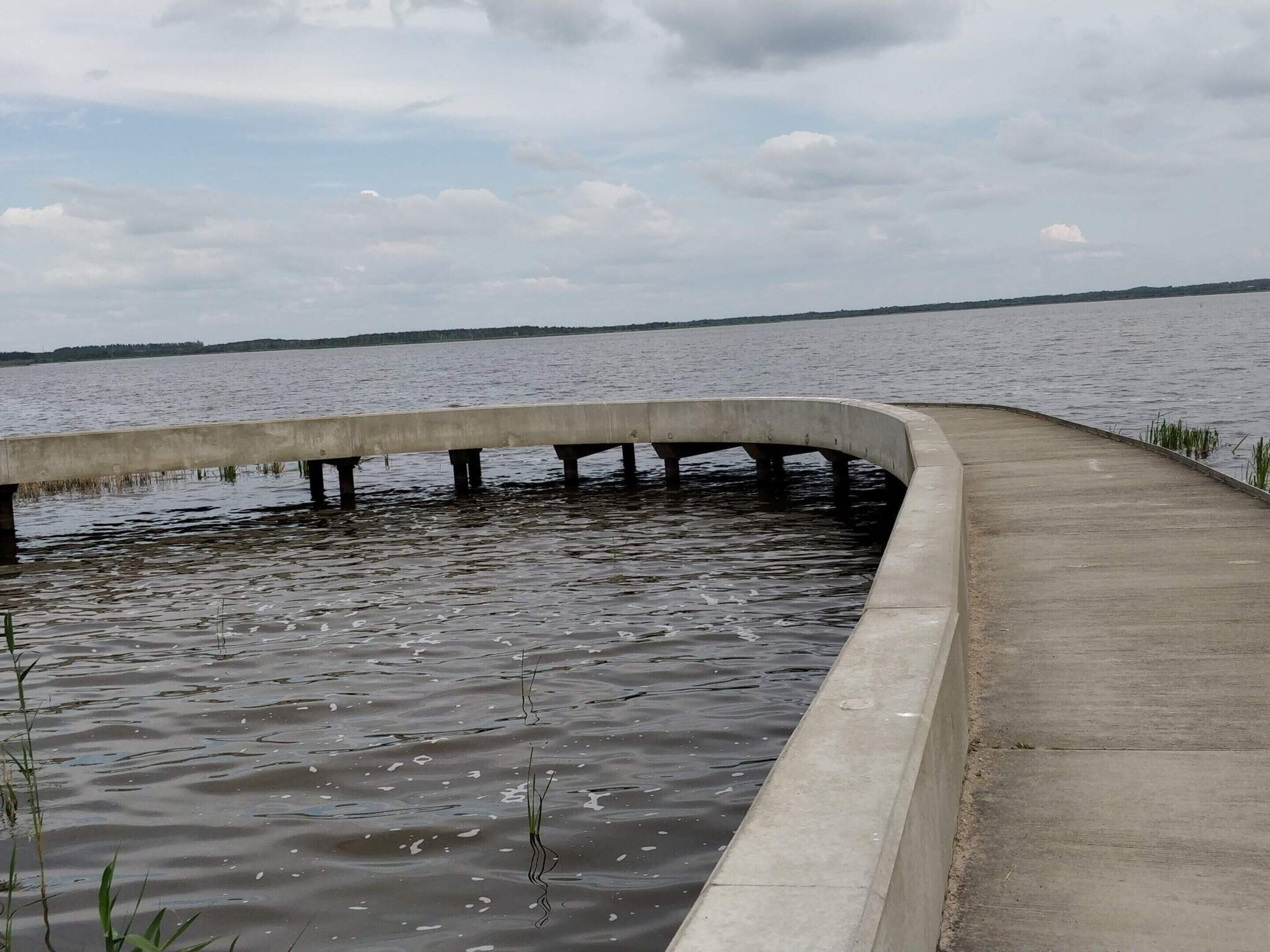 A concrete walkway extending over water with a curved edge, leading to a distant shoreline.