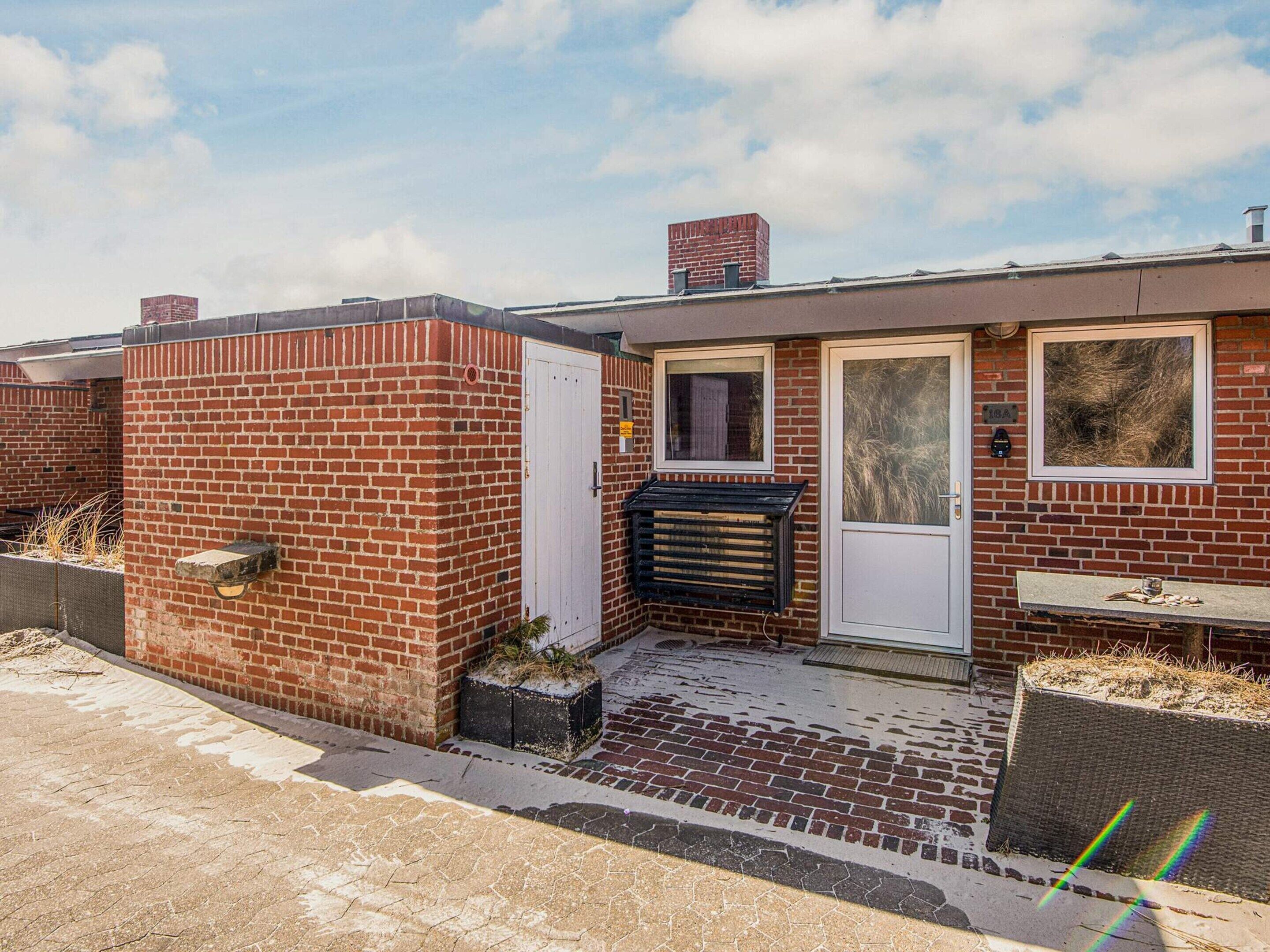 Een rode bakstenen huis met een witte deur, een klein raam en een schoorsteen.