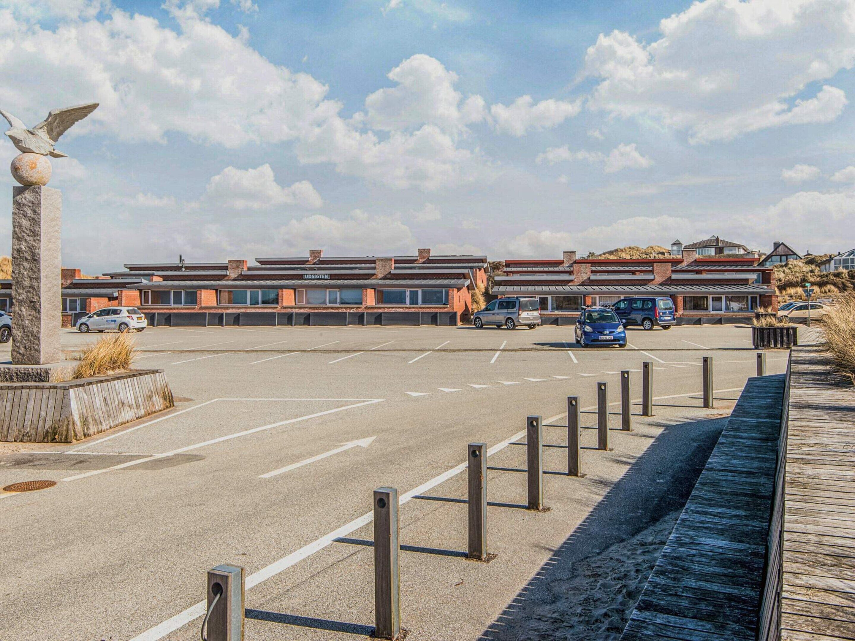 A parking lot with a row of cars, a building with a sign 'UDSIGHTEN', and a statue of an eagle.