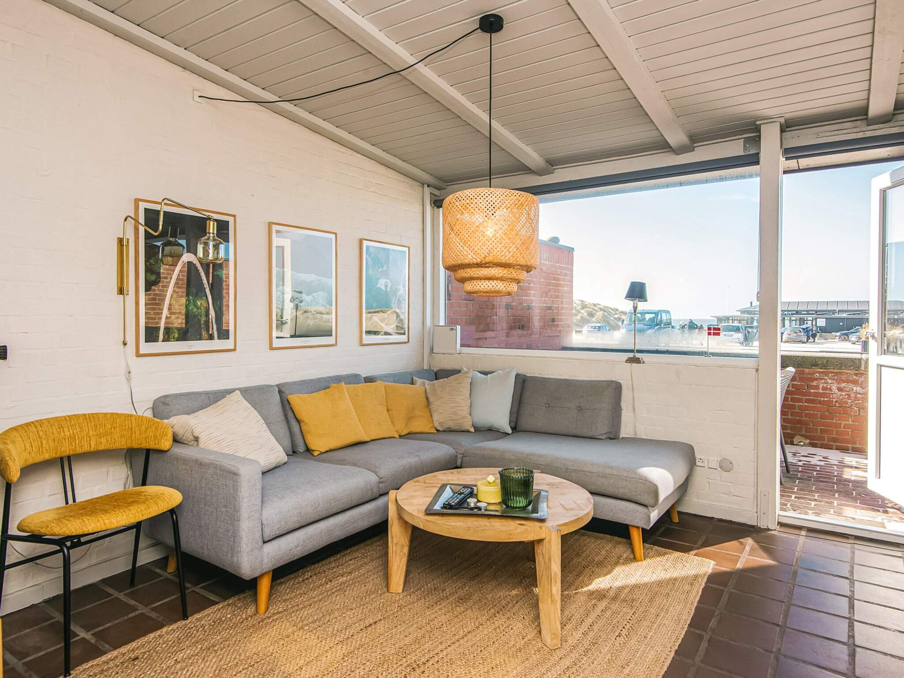 A modern living room with a gray sectional sofa, a yellow chair, a round coffee table, and a large window offering a view of the outside.