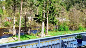 A deck with a white railing overlooking a river and forested area. - 8 Person Holiday Home in Lindesnes (Lindesnes)