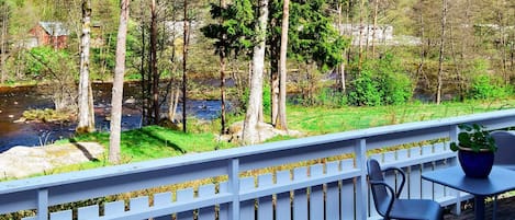 A deck with a white railing overlooking a river and forested area.