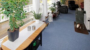 A cozy room with a wooden table, potted plants, a black leather chair, and a vintage stove. - 8 Person Holiday Home in Lindesnes (Lindesnes)