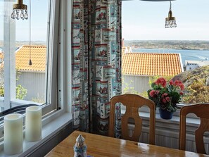 A room with a view of a coastal landscape, a table with candles, and a potted plant with flowers. - 3 Person Holiday Home in Gullholmen (Gullholmen)