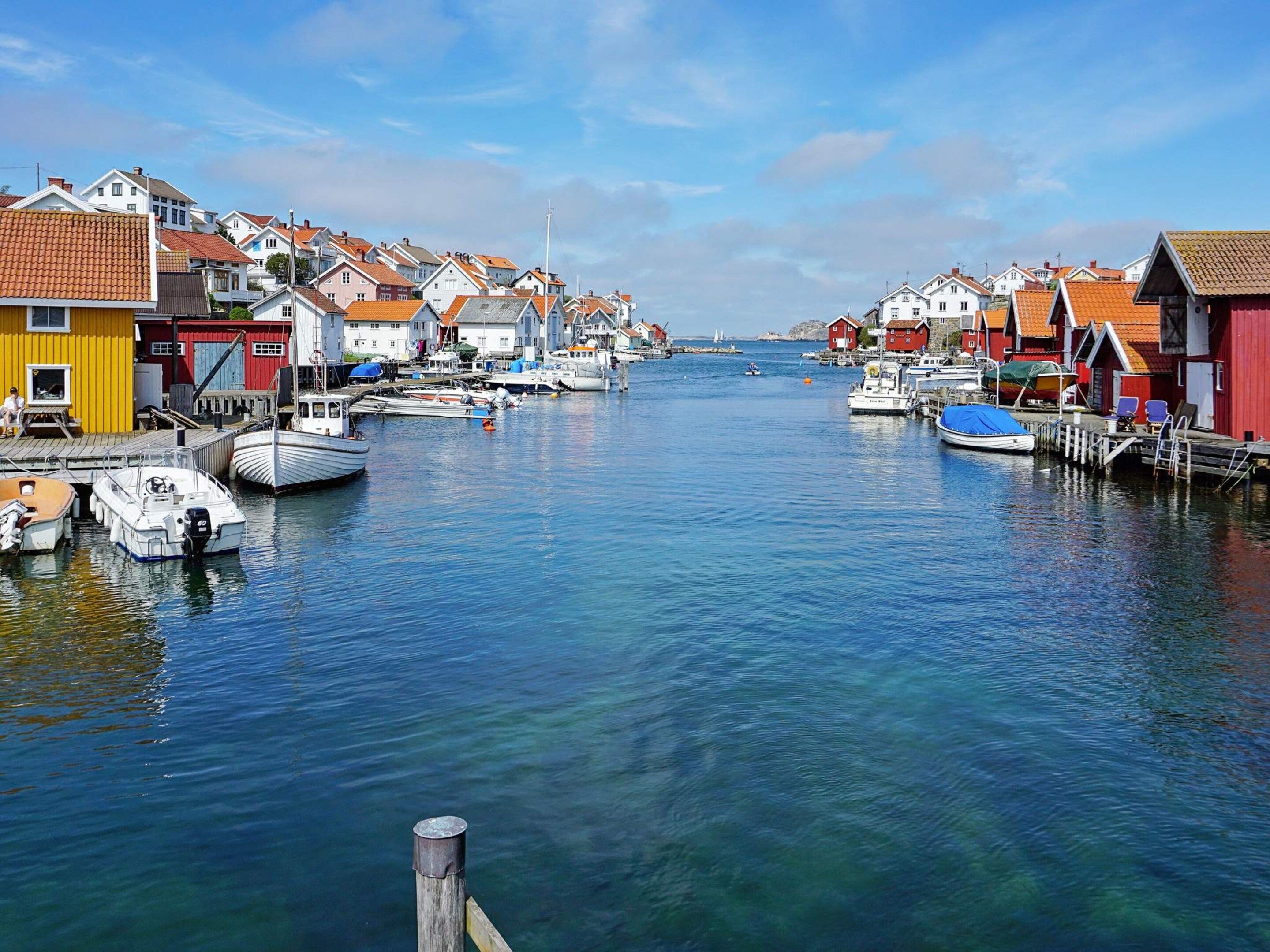 A harbor with boats docked, wooden houses with red roofs, and a clear blue sky.