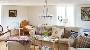 A cozy living room with a wooden floor, a sofa, a coffee table, a chair, a bed, and a chandelier. - Holiday Home in Gamleby (Gamleby)
