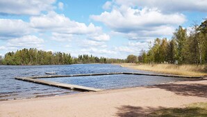A lakeside area with a sandy beach and wooden docks extending into the water. - Holiday Home in Gamleby (Gamleby)