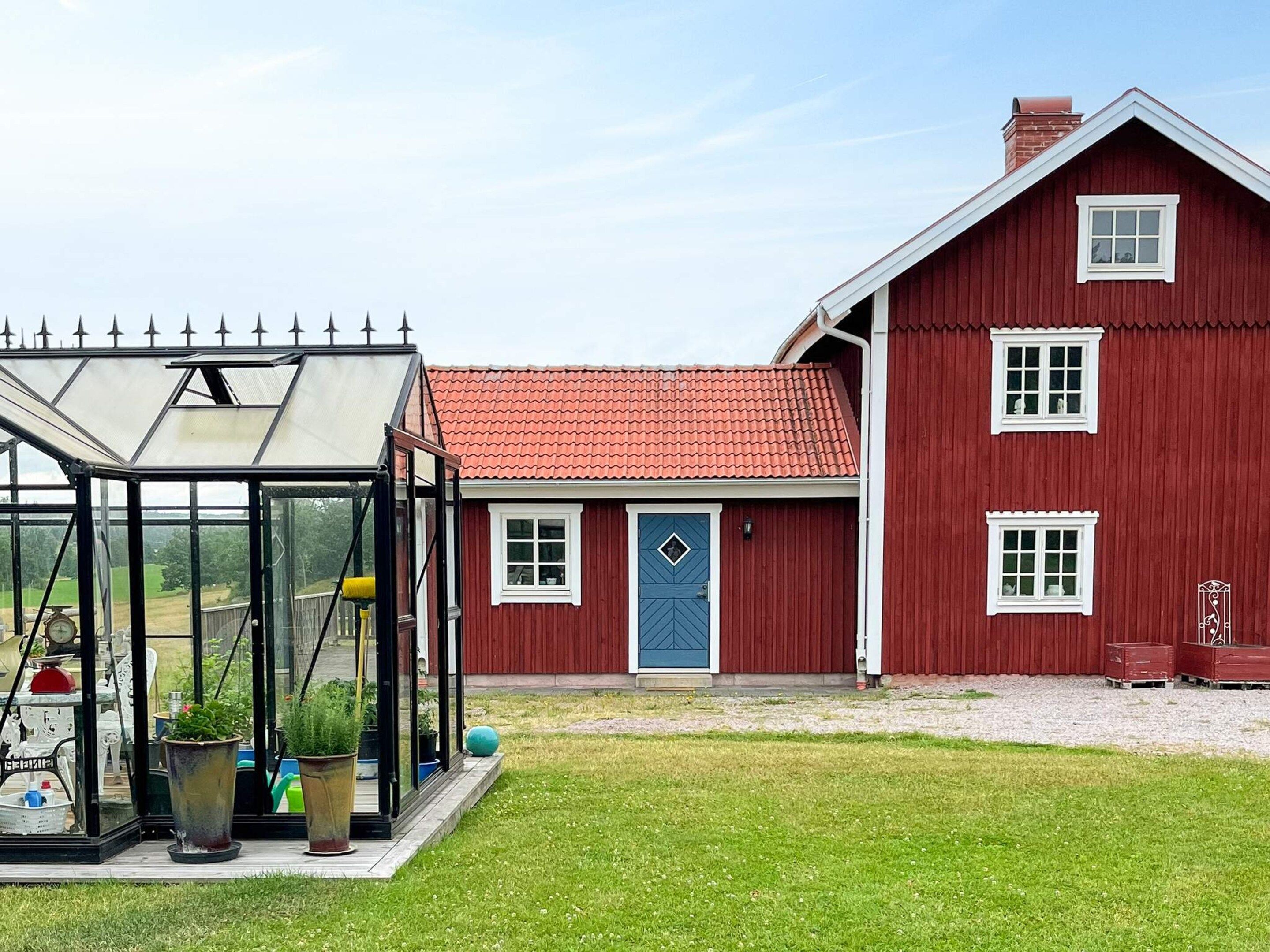 A red barn with a blue door, a glass greenhouse, and a gravel driveway.