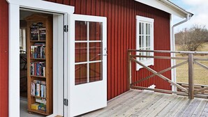A red barn with a wooden deck, a white door, and a window. - Holiday Home in Gamleby (Gamleby)