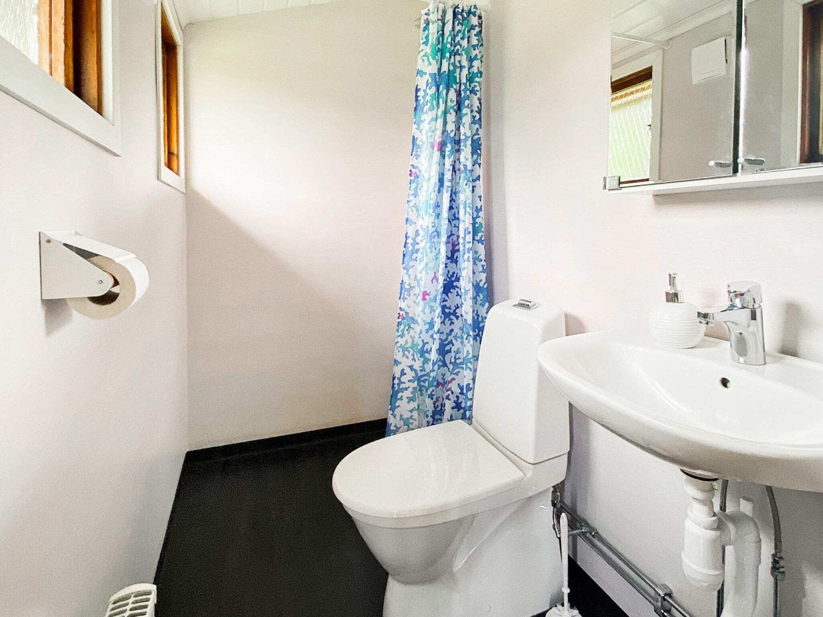 Een badkamer met toilet, wastafel, douchegordijn en spiegel.