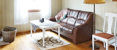 A furnished room with a brown leather sofa, a white armchair, a small table, a lamp, and a patterned rug.