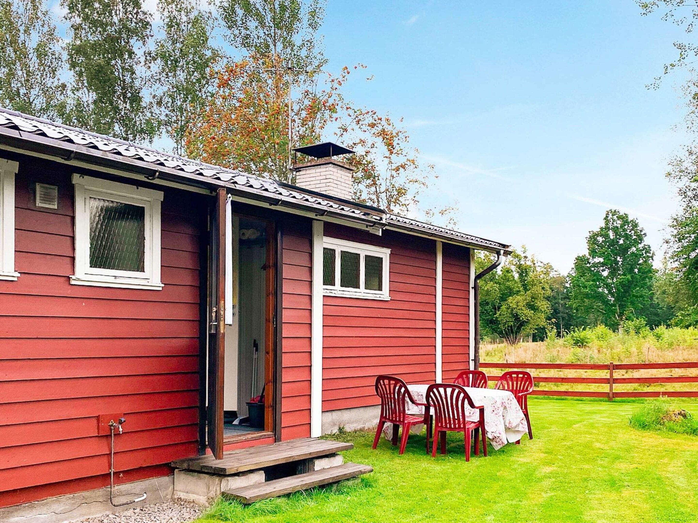 A red wooden house with a porch, a table with chairs, and a grassy yard.