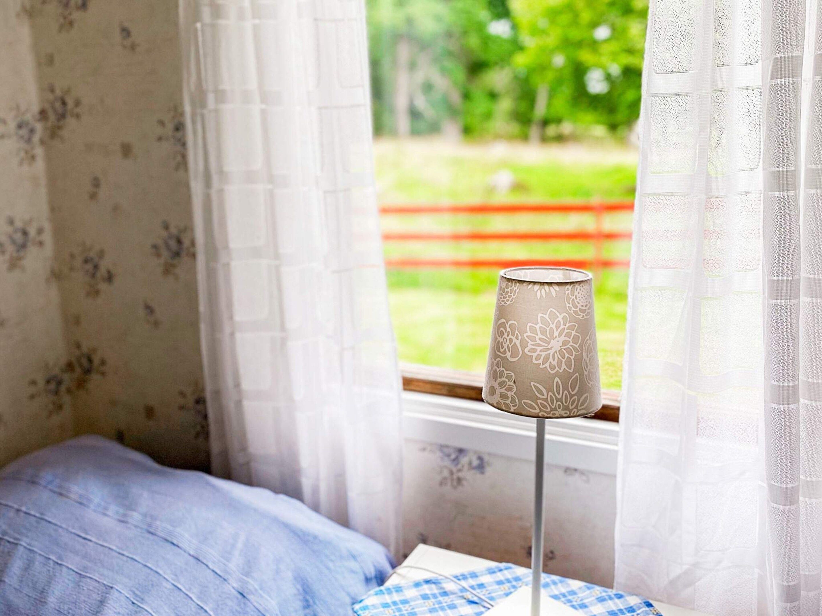 A room with a bed, a lamp, and a window with curtains.