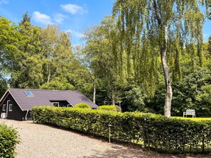A black building with a sloped roof, surrounded by well-maintained hedges and trees.