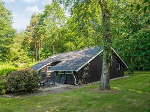 A cabin with a sloped roof, surrounded by dense greenery and trees.