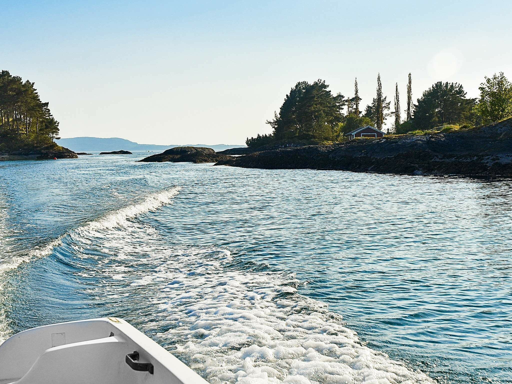 A boat moving through a calm river with rocky shores and trees on both sides.