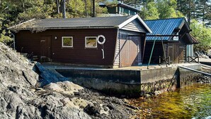 A wooden cabin with a metal roof, situated on a rocky shore with a dock extending into a body of water. - 5 Person Holiday Home in OS (Bjørnafjorden)