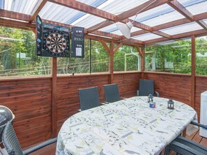 Un espace extérieur abrité comprenant un jeu de fléchettes, une table avec des chaises et une vue sur la verdure.