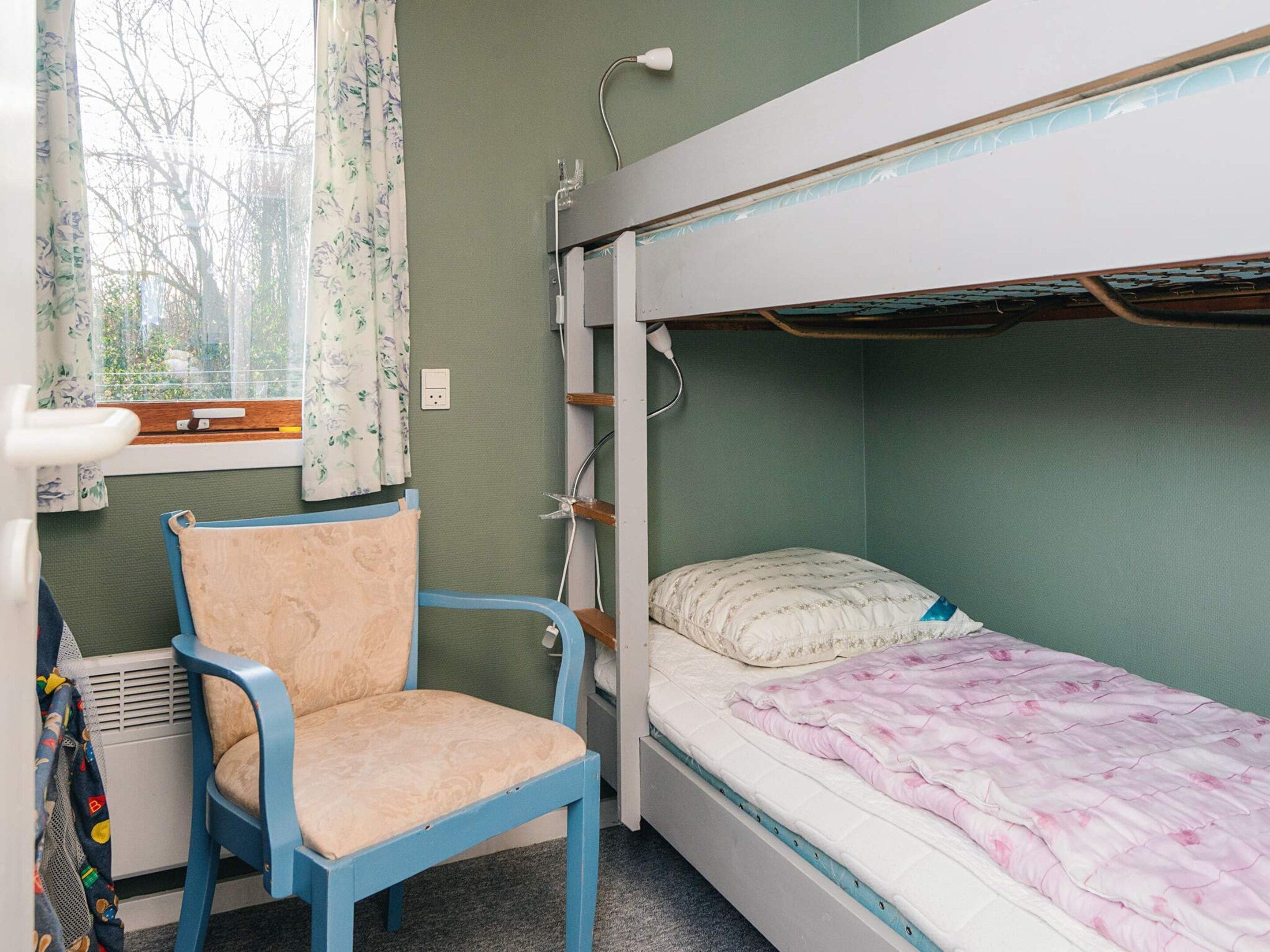 A room with a bunk bed, a chair, a window with curtains, and a radiator.