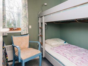 Una habitació amb literes, una cadira, una finestra amb cortines i un radiador.