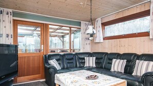 A cozy living room with a black leather sofa, a wooden coffee table, and a television. - 4 Person Holiday Home in Juelsminde (Horsens)