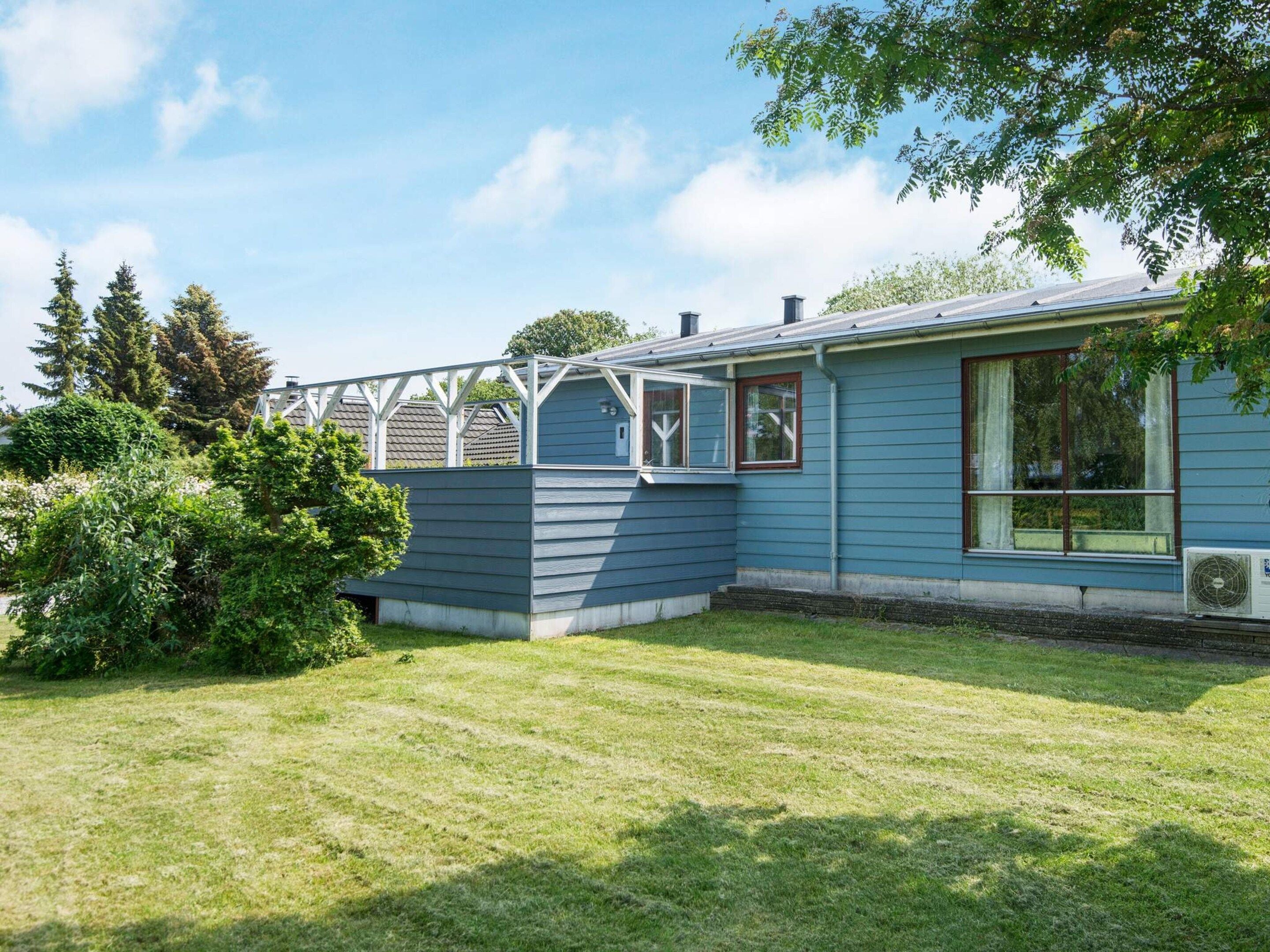 Een gelijkvloers huis met een overdekte veranda, een gazon en een grote boom.