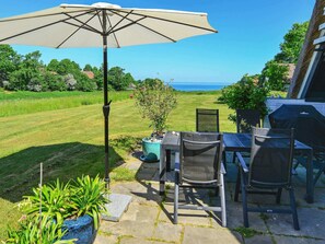 Eine Terrasse mit Tisch und Stühlen, einem großen Sonnenschirm und Blick auf das Meer.