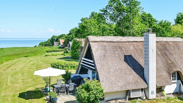 A thatched-roof house with a patio, outdoor seating, and a view of the sea. - Idyllic Holiday Home in Funen near Sea (Middelfart)