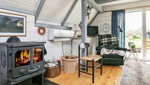 A cozy living room with a wood-burning stove, a comfortable sofa, and a large window offering a view of the outdoors. - Idyllic Holiday Home in Funen near Sea (Middelfart)