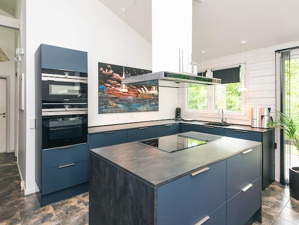 Una cocina moderna con una isla central, hornos integrados y un amplio ventanal.