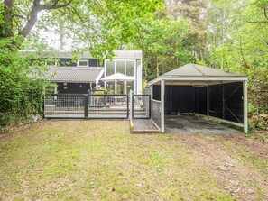 A fenced outdoor area with a covered structure, a building with a tiled roof, and a garden.