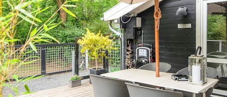 Une terrasse extérieure avec une table et des chaises, un barbecue et une pergola décorée de guirlandes lumineuses.
