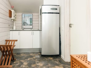 Una cocina compacta con armarios blancos, un refrigerador de acero inoxidable, un banco de madera y suelo de baldosas.