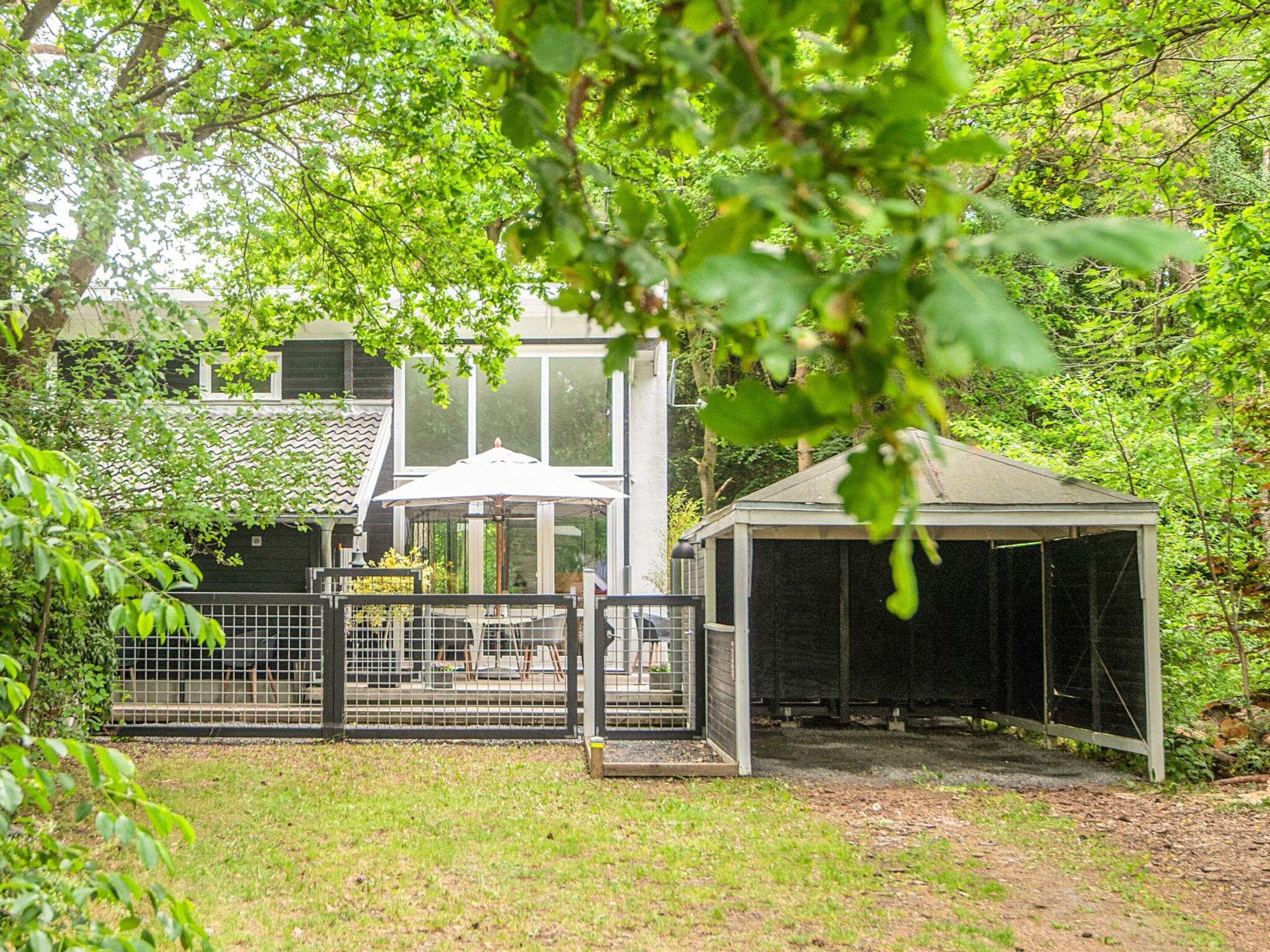 A fenced outdoor area with a covered seating area and a building with a tiled roof.