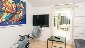 A living room with a treadmill, a flat-screen TV, a painting, and a sofa. - 5 Star Holiday Home in Ronde (Ronde)