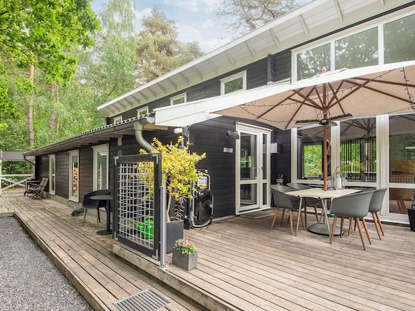A modern outdoor patio area with a dining table and chairs, a covered seating area, and a wooden deck.