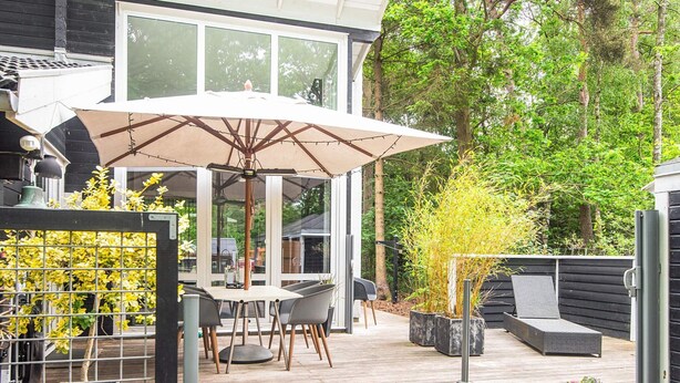 A deck with a table and chairs, an umbrella, and potted plants. - 5 Star Holiday Home in Ronde (Ronde)