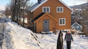 A wooden house with a snow-covered yard and a person standing in front. - 6 Person Holiday Home in Skorovatn (Namsskogan)