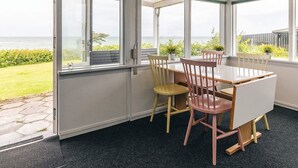 A dining area with a table and chairs, large windows with a view of the sea, and a ceiling light.